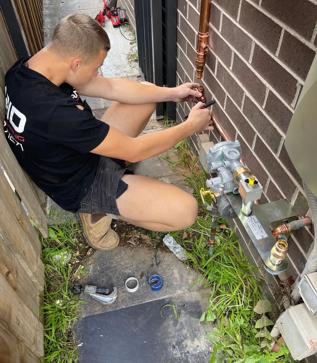 Licensed gas fitter working on a gas meter against a brick wall