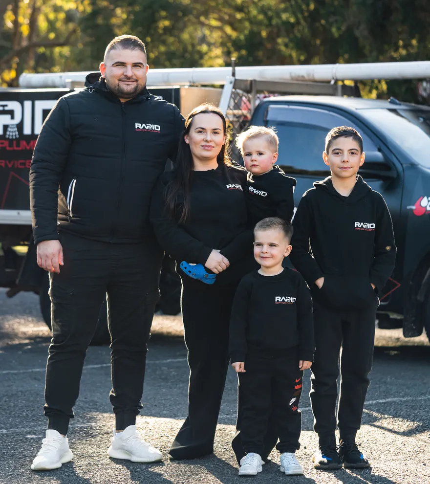The Rapid Service Plumbing owner and his family in branded uniform beside a company ute