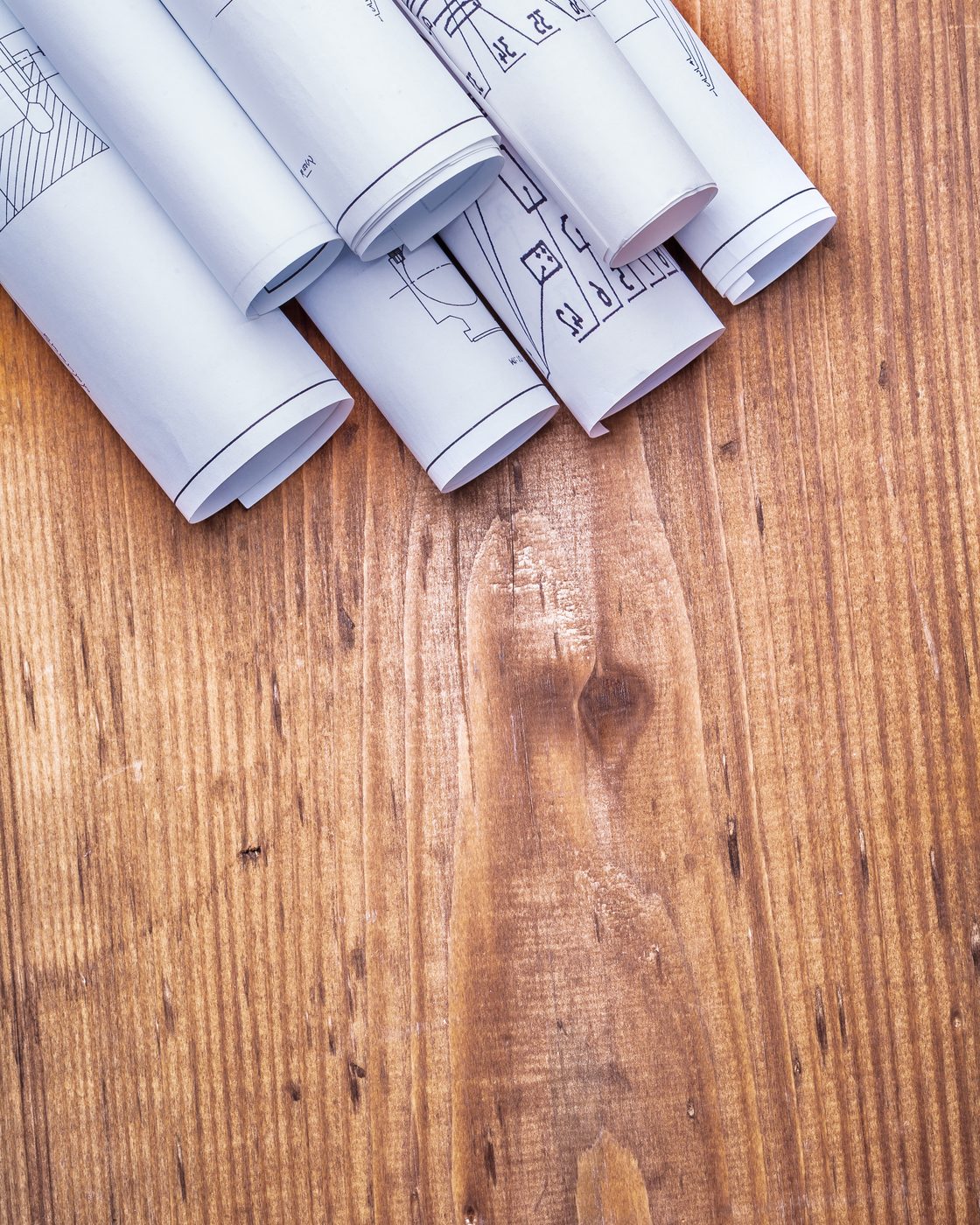 Rolled construction drawings resting on a warm wooden board