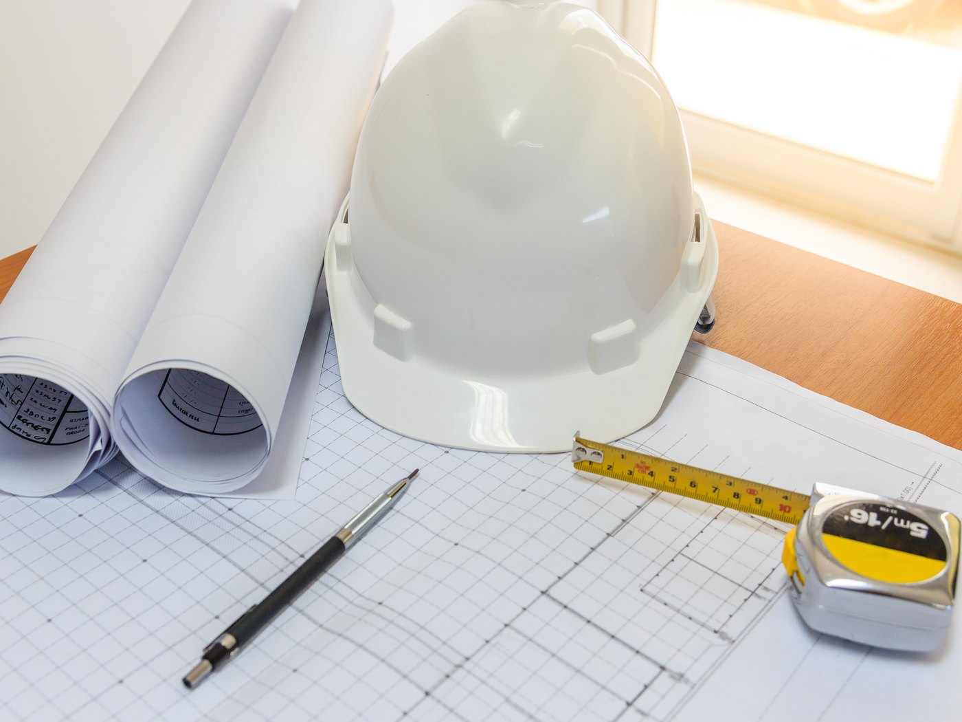 Rolled site plans, a hard hat and a tape measure on a drawing sheet