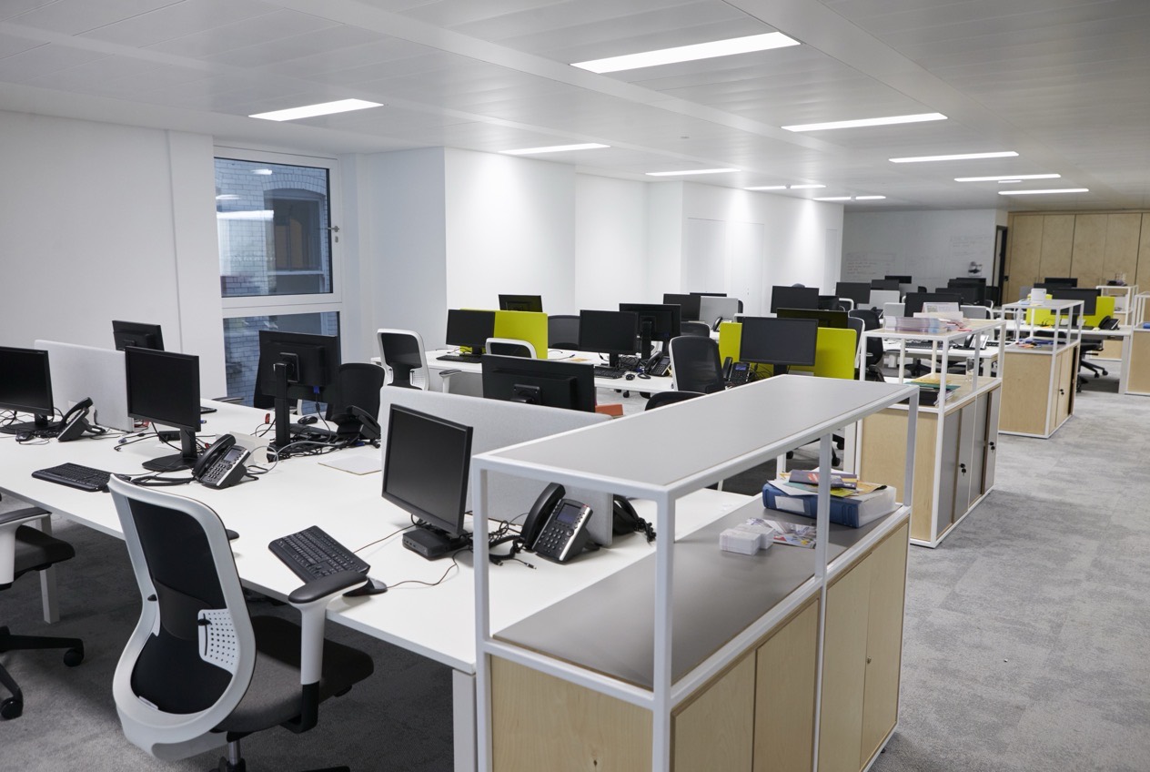 Open plan business office with desks and monitors, empty, in early evening light