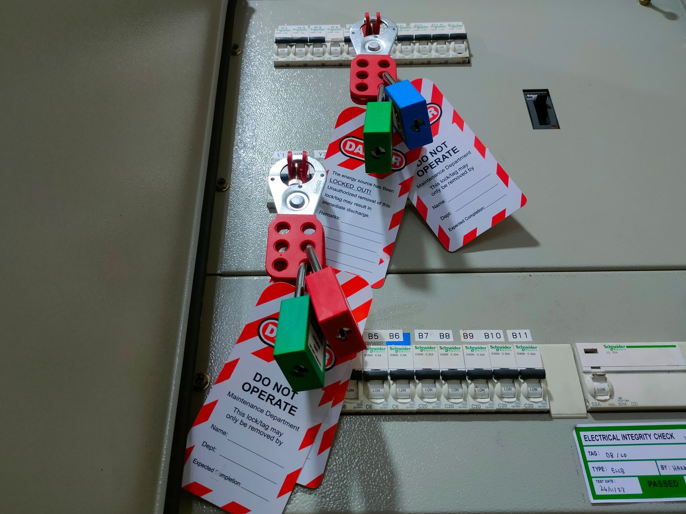 Lockout padlocks and do-not-operate tags on a switchboard, beside a dated electrical integrity check card
