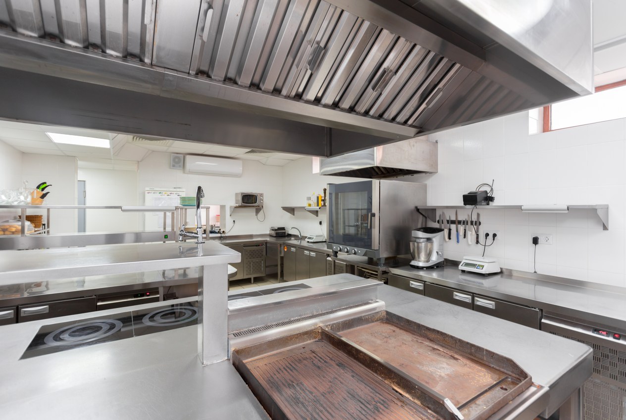 Empty commercial kitchen with a stainless extraction canopy and steel benches